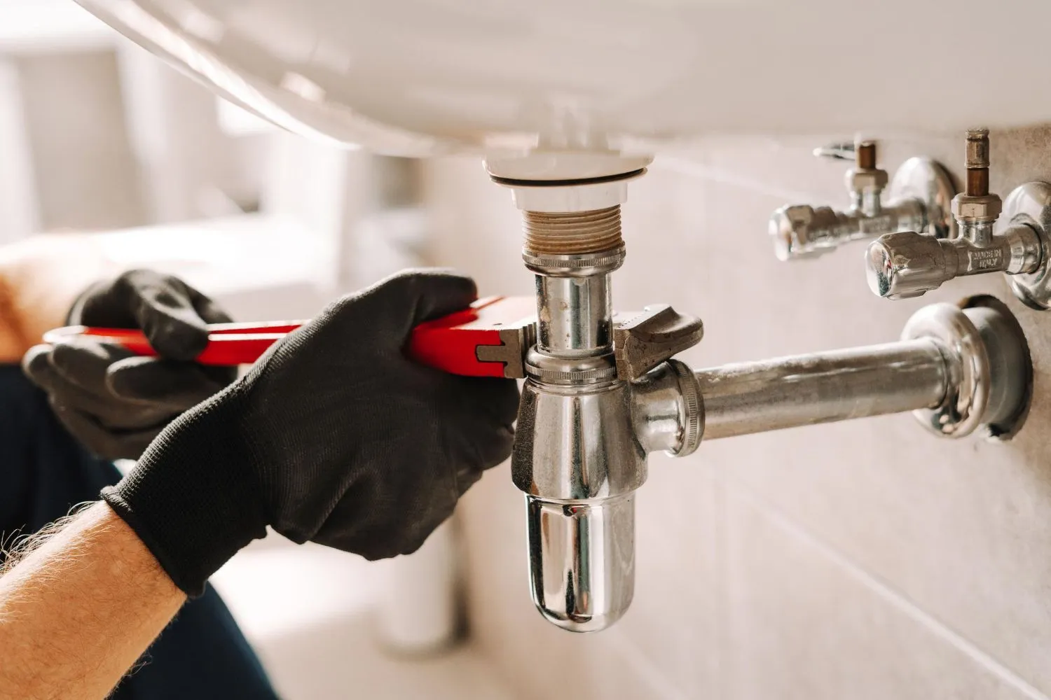 A plumber is fixing a sink pipe with a wrench.