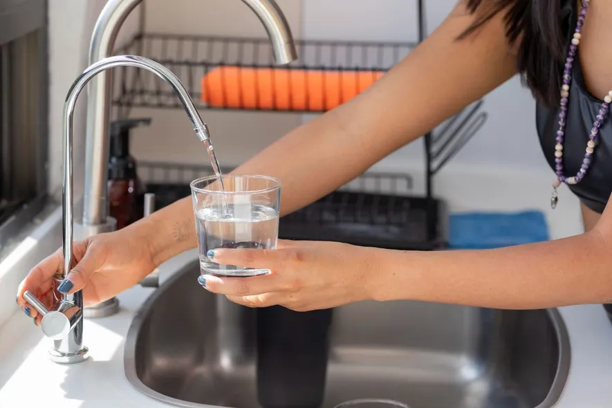 A woman is pouring water into a glass in a kitchen sink, water treatment systems