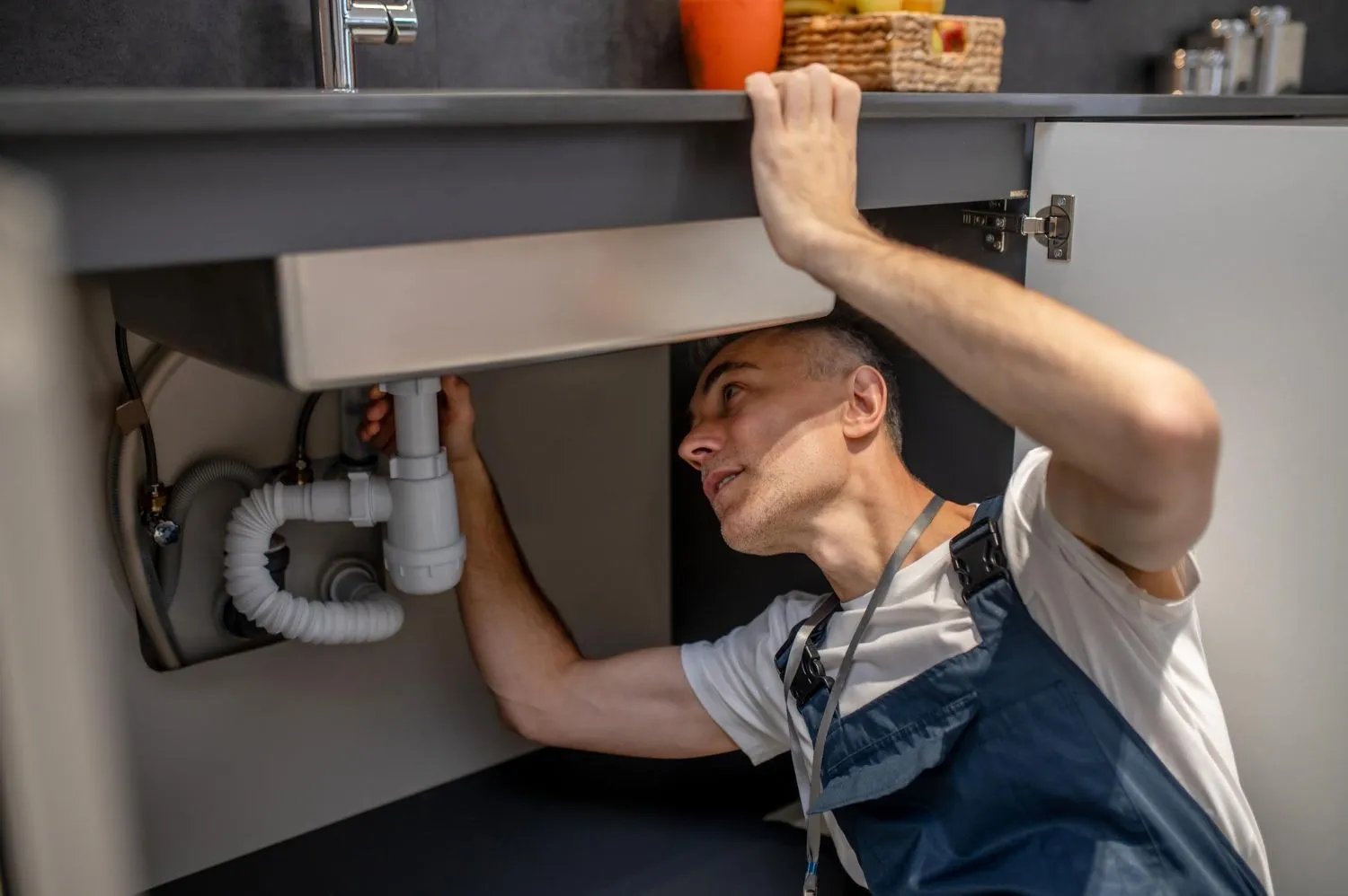 A plumber is fixing a sink in a kitchen.