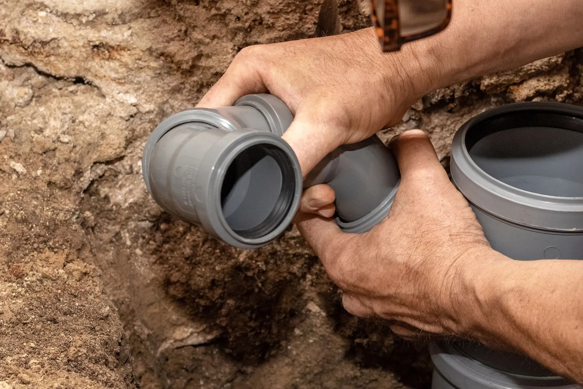 A man is fixing a drain pipe in the dirt.