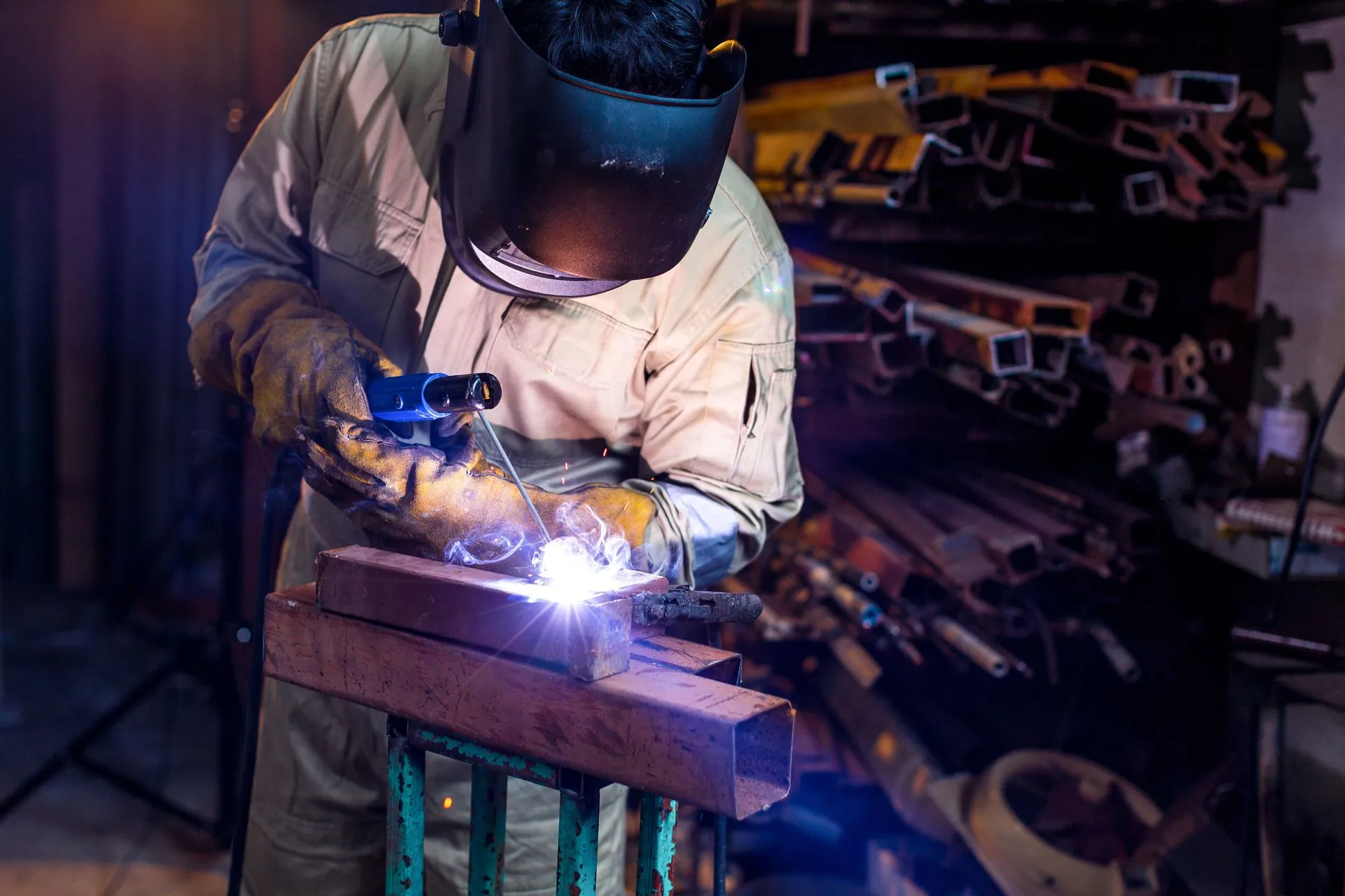 A man is welding a piece of metal in a workshop.